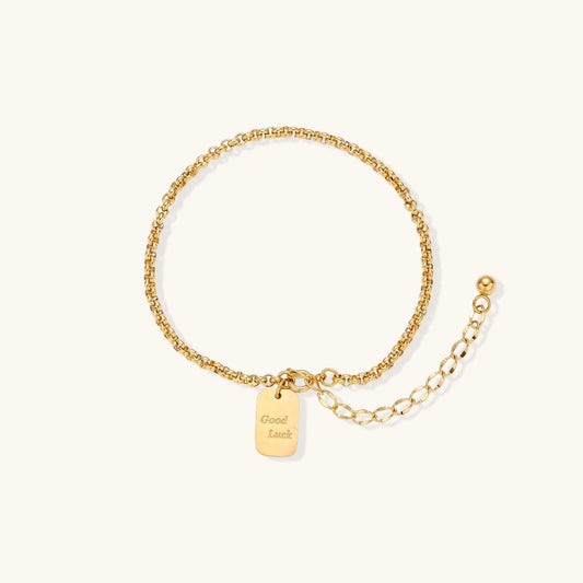 Delicate 18K gold-plated chain bracelet with Good Luck engraved rectangular pendant on cream background