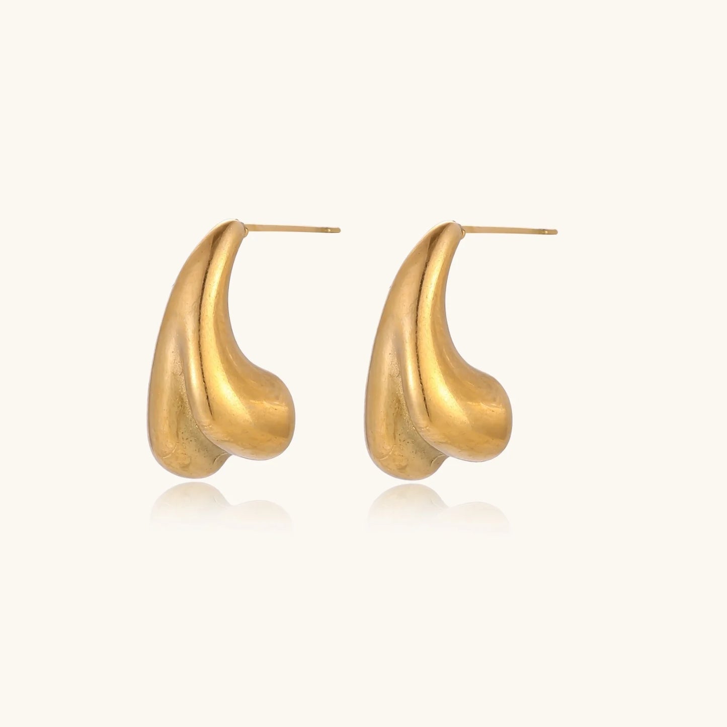 Pair of sculptural gold stud earrings with twisted organic forms on cream background